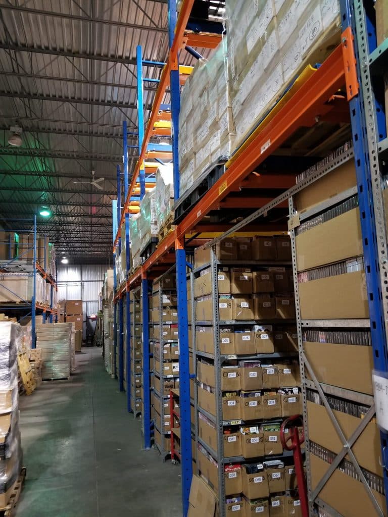 Allée de racks chez Les Services Système D : palettes en hauteur et bacs de prélèvement identifiés par emplacement numéroté